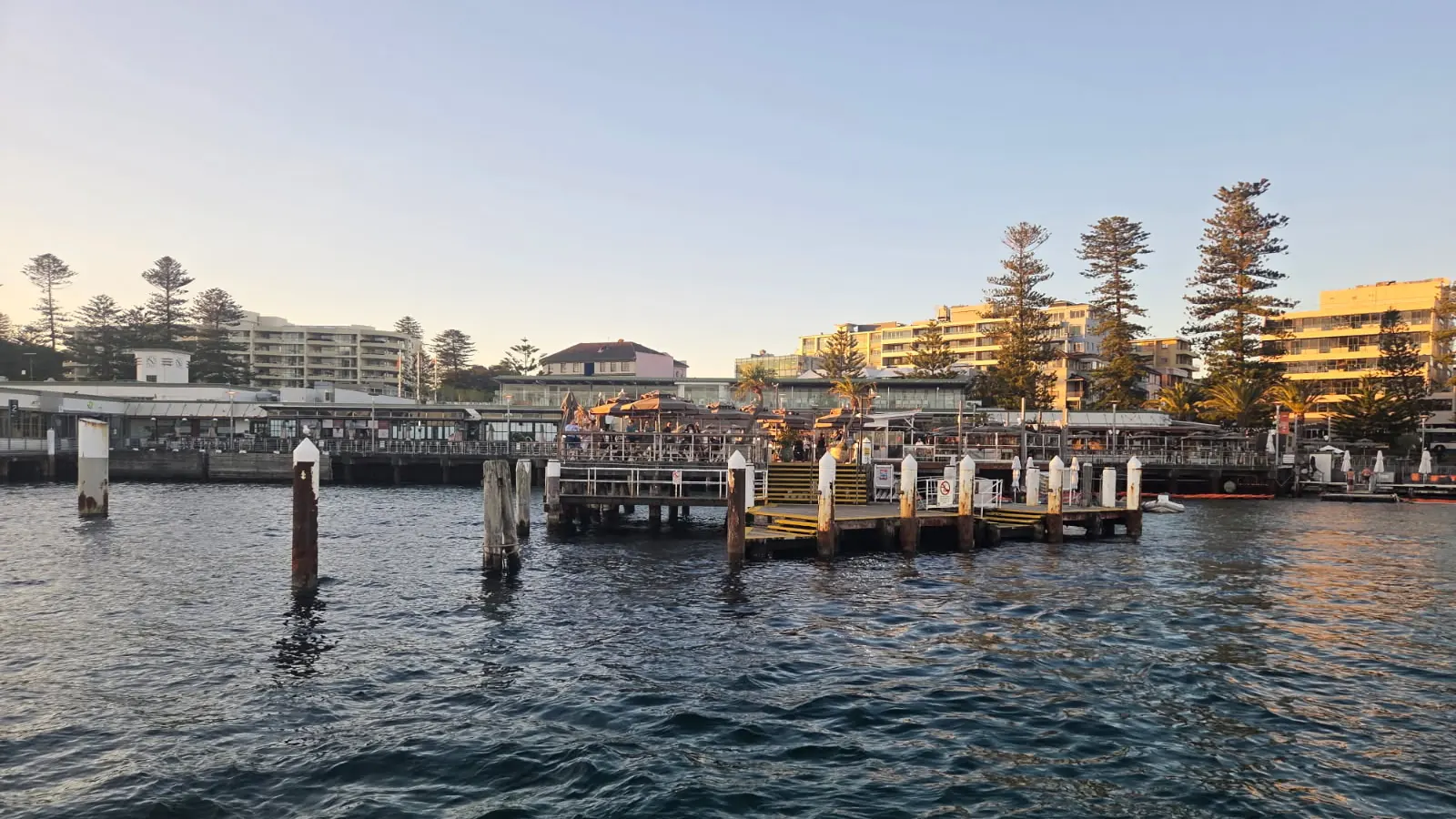 Manly Wharf at sunset seen from Sydney Harbour, with the ferry wharf pontoon and waterfront dining terraces